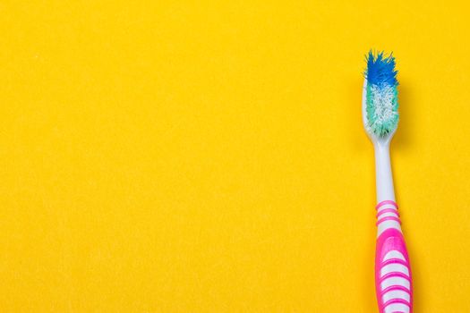 Old used toothbrush on the yellow background. Top view