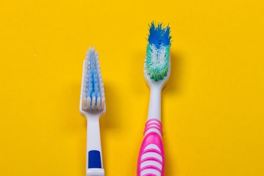 Old used and new toothbrushes on the yellow background. Top view