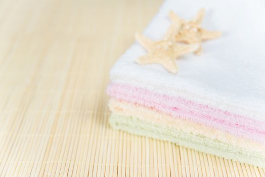 Stack of multicolored clean terry towels on a mat and two starfish, with space for text