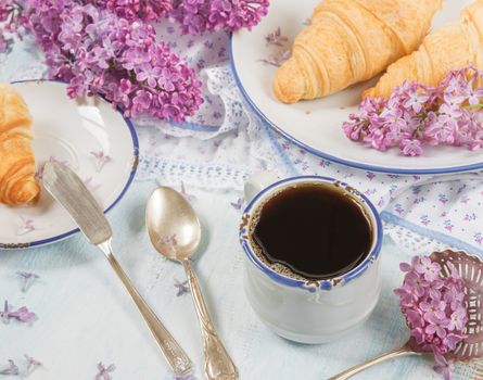 Spring breakfast with a cup of black coffee, croissants and lilac flowers