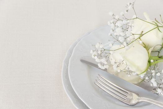 Beautiful decorated table with empty white plates, cutlery and white rose flowers on tablecloths, with space for text