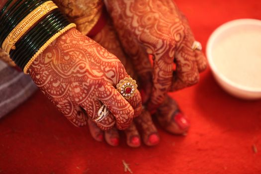 A hindu bride adjusting the traditional ring in her feet with her hand having beautiful mehendi design
