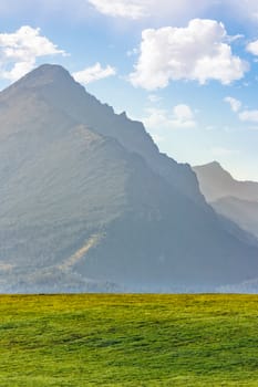 high rocky peak of Tatra mountains in evening haze behind the green field