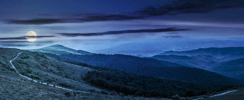 panoramic summer landscape with road through hillside meadow in mountains at night in full moon light