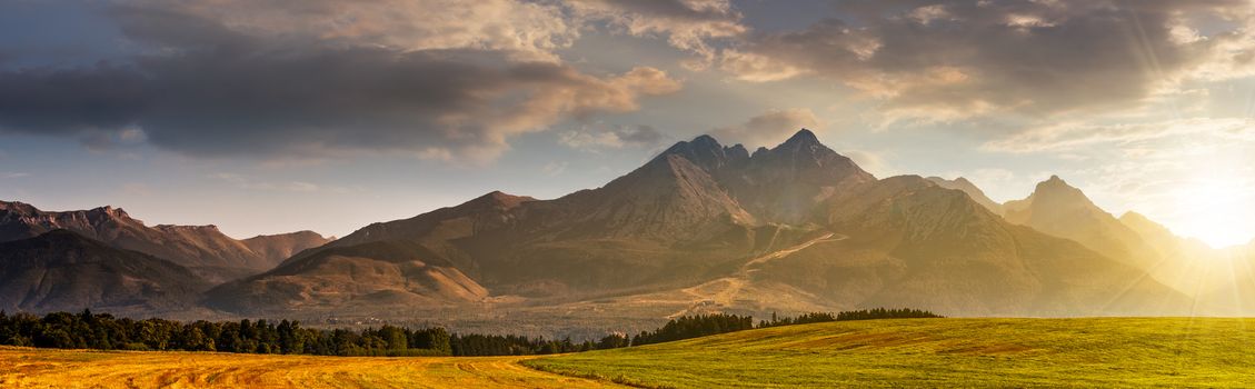 panorama of Tatra mountains in haze behind the forest and rural field in morning light 