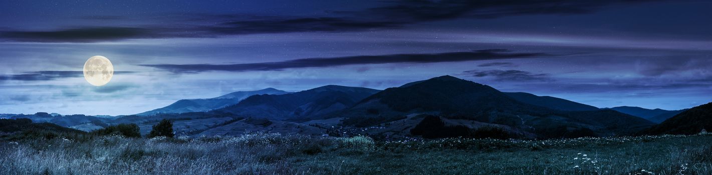 Summer landscape panoramic image of rural fields in mountains under cloudy sky at night in full moon light