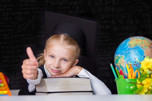 Gilr in graduation cap showing ok sign on blackboard background