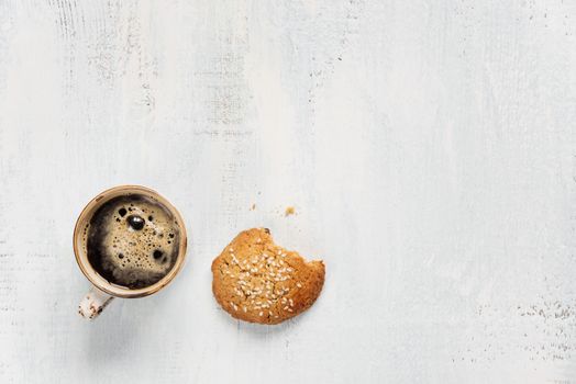 Black coffee with crema in vintage porcelain cup and oatmeal cookie on a light wooden background, with space for text, top view