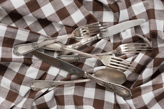 Silverware on a creasy white and brown checked cotton fabric closeup