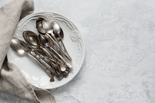 Various silverware on a ceramic plate on the background of gray concrete surface, with copy-space