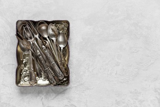 Various silverware in a metal tray on the background of gray concrete surface; with copy-space