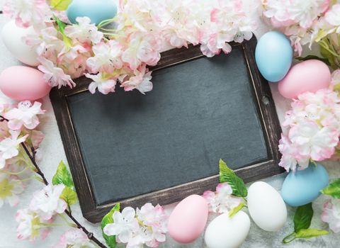 Easter card with old blank chalkboard surrounded by pink flowers and colorful Easter eggs