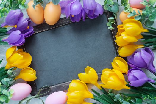 Easter card with old blank chalkboard surrounded by yellow and purple crocus flowers and colorful Easter eggs