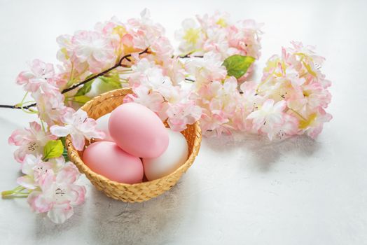 Easter card with pink and white easter eggs in a wicker basket on the background of delicate pink flowers of the cherry blossoms