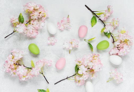 Beautiful delicate Easter composition with pink cherry flowers and multicolored Easter eggs on the stone background, top view, flat lay