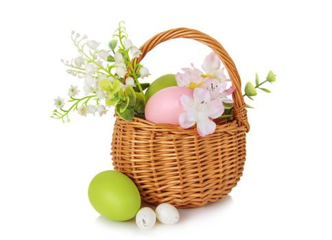 Wicker basket with pink and green Easter eggs as well as with lilies of the valley and other flowers isolated on white background
