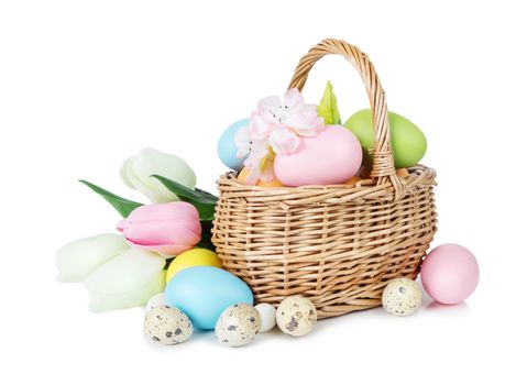Wicker basket with pink, blue and green Easter eggs as well as with tulips and other flowers isolated on white background