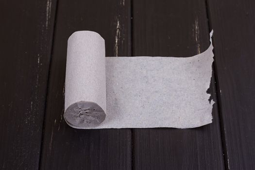 The roll of grey toilet paper on the black wooden background