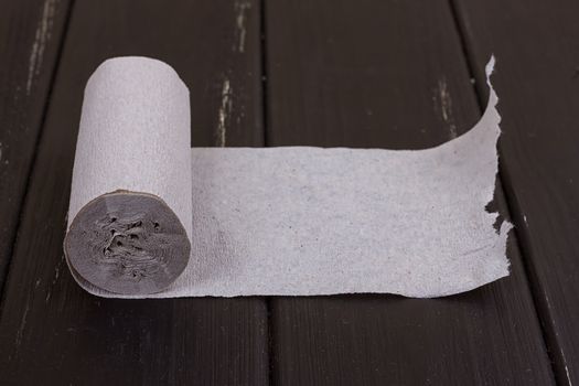 The roll of grey toilet paper on the black wooden background