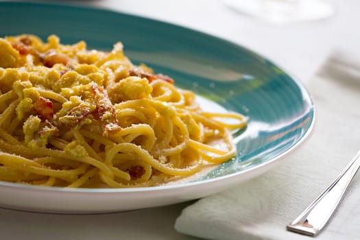 Closeup of spaghetti carbonara with egg, smoked bacon and cheese over a table