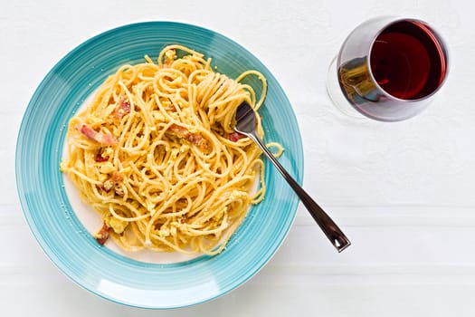 Spaghetti carbonara on with egg, smoked bacon and cheese over a table with a red wine glass seen from above