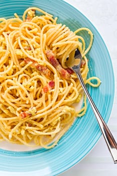 Closeup of spaghetti carbonara on fork with egg, smoked bacon and cheese over a table seen from above