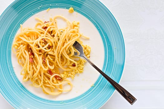 Closeup of eaten spaghetti carbonara with egg, smoked bacon and cheese over a table seen from above