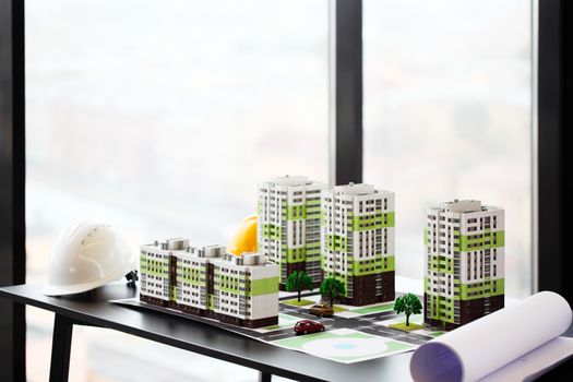 Model of residential quarter and hardhats on table in office