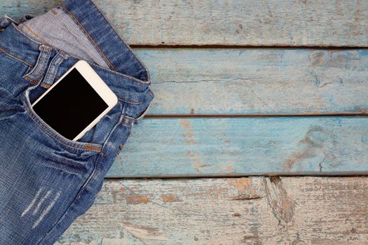 Touch smartphone-phone with headphones in jeans pocket on blue wooden background.