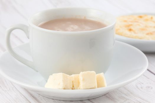 Cup of hot chocolate with cheese and arepa served in white dishware