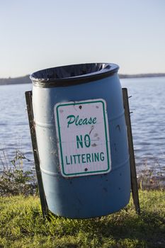 No littering sign on an empty garbage can on a lakeshore