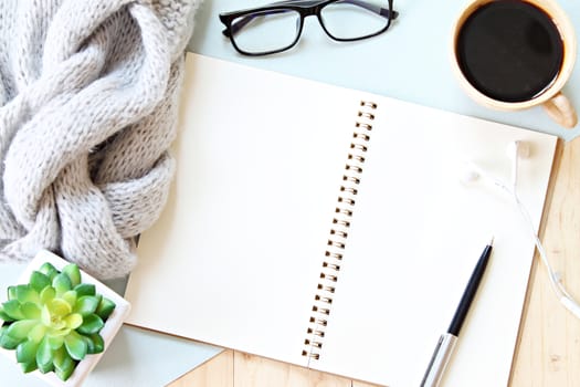 Business, weekend, holiday or good morning concept : Flat lay or top view of gray knitted scarf, open blank notebook paper, coffee cup and eyeglasses on wooden background