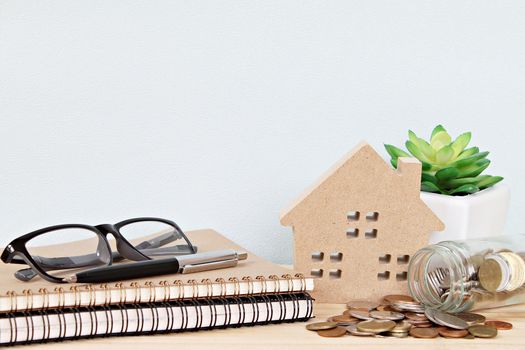 Business, finance, saving money, property loan or mortgage concept :  Wood house model and coins scattered from glass jar on office desk table