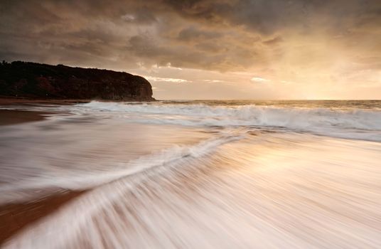 The backflow of two waves zip together.  Exposure showing  motion of the water and illusion of painted affect in the other waves.  Moody skies above drizzle occasionally and a gentle light warms the underside.  Basin Beach, Mona Vale