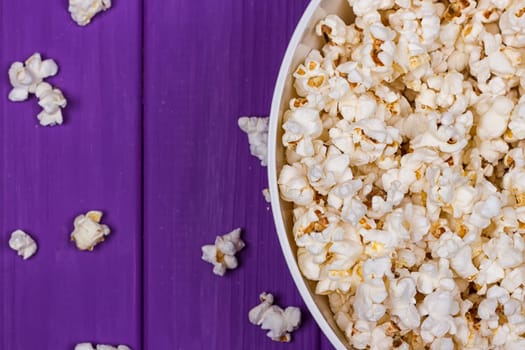 Popcorn in a bowl on purple wooden surface