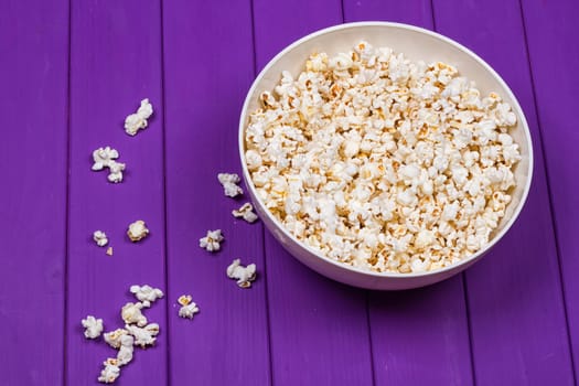 Popcorn in a bowl on purple wooden surface