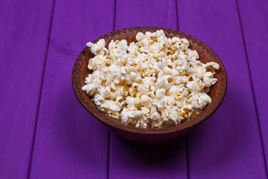 Popcorn in a bowl on purple wooden surface