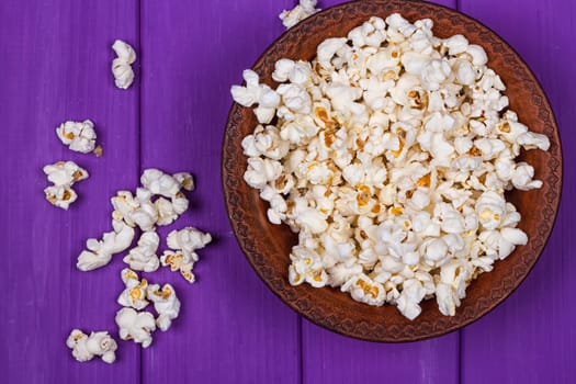 Popcorn in a bowl on purple wooden surface