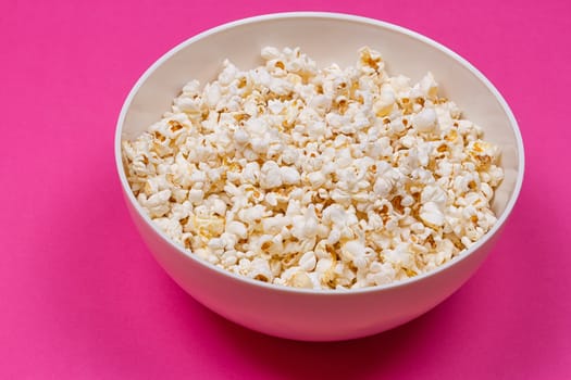 Bowl of Delicious Popcorn spilling onto a pink background