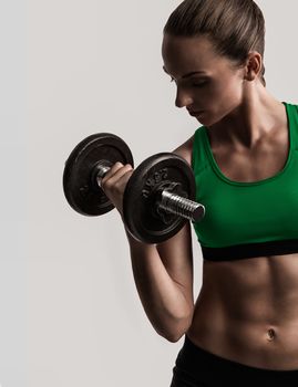 Beautiful young woman in a workout gear lifting dumbbells