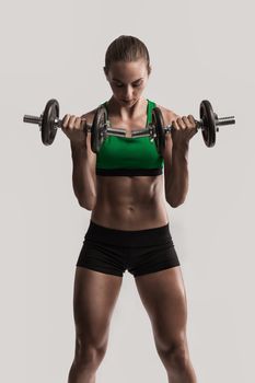 Beautiful young woman in a workout gear lifting dumbbells