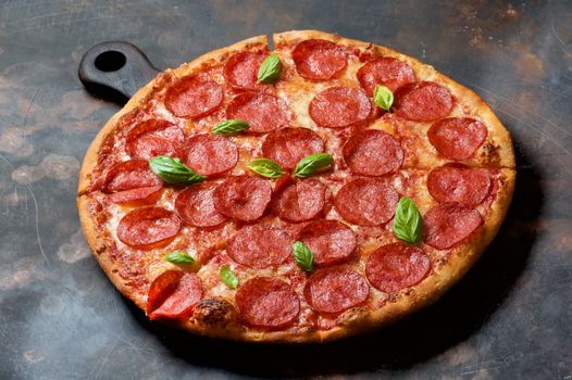 Freshly Baked Pepperoni Pizza with Tomatoes, Pepperoni, Cheese and Basil on Cutting Board closeup on Grunge background
