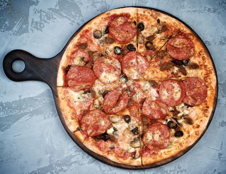 Freshly Baked Homemade Meat Pizza with Salami, Meat Balls, Ham, Black Olives and Mozarella Cheese on Serving Board closeup on Grey Textured background. Top View