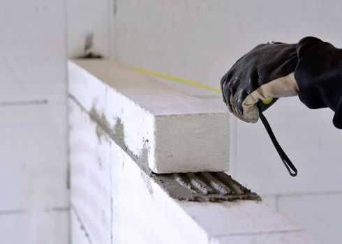 The bricklayer measures a newly built wall with a tape measure.