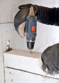 The bricklayer using a battery screwdriver for drilling a screw into a concrete aerated blocks wall. 