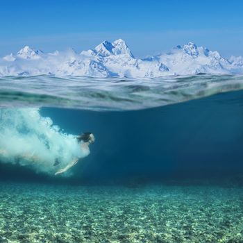 Man swimming underwater in blue transparent sea water, snow mountains on background