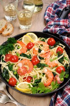Pasta with fried prawns, peas, tomatoes and spinach in a frying pan, on a table with cider glasses.