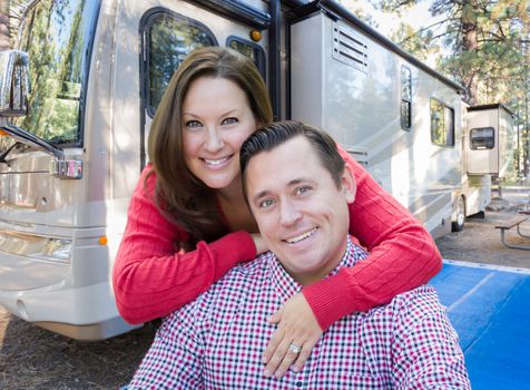 Happy Caucasian Couple In Front of Their Beautiful RV At The Campground.