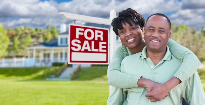 Happy African American Couple In Front of Beautiful House and For Sale Real Estate Sign.