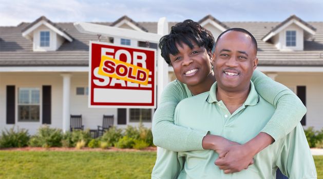 Happy African American Couple In Front of Beautiful House and Sold For Sale Real Estate Sign.